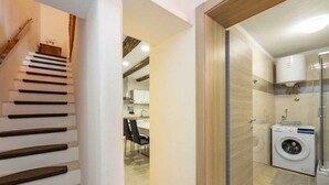 A modern kitchen with a built-in washing machine, a dining area with chairs, and a staircase with wooden steps.
