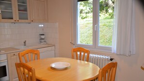 Eine Küche mit einem runden Holztisch, vier Holzstühlen, einer weißen Spüle und einem Fenster mit Blick auf eine Rasenfläche.