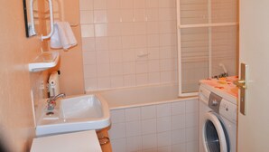 Ein Badezimmer mit Waschbecken, Spiegel, Handtuchhalter, Dusche und einer Waschmaschine.