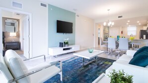 Een moderne woonkamer met een flatscreentelevisie, witte banken, een salontafel en een blauw vloerkleed.