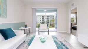 Een moderne woonkamer met een witte bank, een glazen salontafel en uitzicht op een balkon met stadsbeeld.