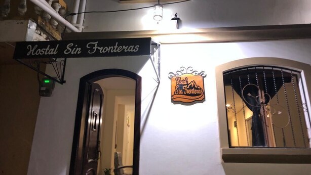 A hotel sign with the name "Hostal Sin Fronteras" and a logo with a mountain and sun. - Hostal Sin Fronteras (León)