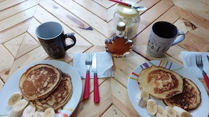 A wooden table with two plates of pancakes, a jar of syrup, and two coffee mugs. - Hostal Sin Fronteras (León)