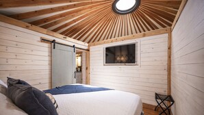A room with a bed, a window, and a wooden ceiling.