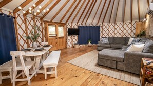 A yurt interior with a wooden dining table, benches, a grey sofa, and a flat-screen TV mounted on the wall.
