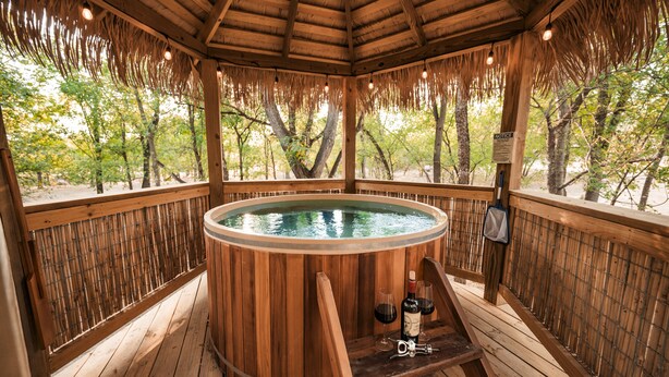 A wooden hot tub with a wooden deck and a view of trees.