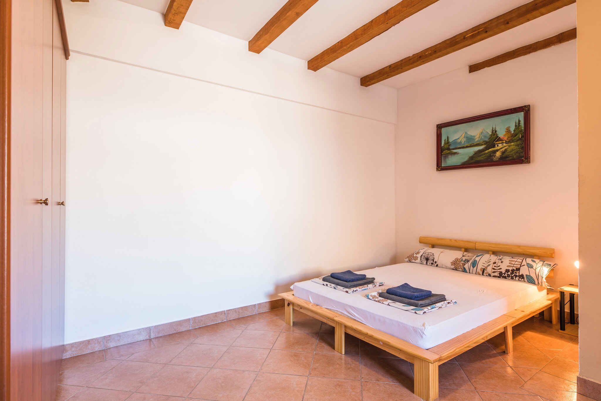 A bedroom with a wooden bed, white walls, a painting, and a tiled floor.