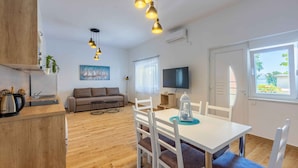 A modern kitchen with a wooden countertop, a dining table with white chairs, a sofa, and a TV mounted on the wall.