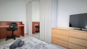 Ein Schlafzimmer mit einem Bett, einem Schreibtisch mit Stuhl, einem Fernseher auf einer Holzkommode und einem Spiegel.