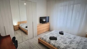 Ein Hotelzimmer mit Bett, Fernseher, Kleiderschrank und Schreibtisch.