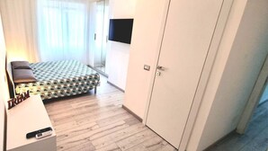 Ein Schlafzimmer mit Bett, einem an der Wand befestigten Fernseher, einem Kleiderschrank und einem Nachttisch mit Fernbedienung.