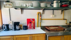 Una cocina con armarios de madera, encimera blanca y varios utensilios, como una cafetera, tazas y una tabla de cortar roja.