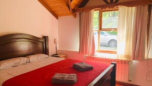 Un dormitorio con una cama de madera, una colcha roja y una ventana con cortinas.
