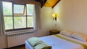 Un dormitorio con cama, ventana con cortinas, lámpara fijada a la pared y suelo de madera.