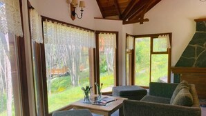 Una habitación acogedora con techo de madera, ventanas amplias con cortinas de encaje, una mesa de centro de madera y una zona de estar confortable.
