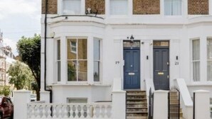 Una casa de dos pisos con fachada blanca, detalles de ladrillo y una puerta principal azul.