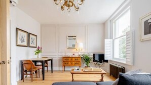 Un salón amplio con un sofá, una mesa de comedor con sillas, un aparador de madera, un televisor y una araña.