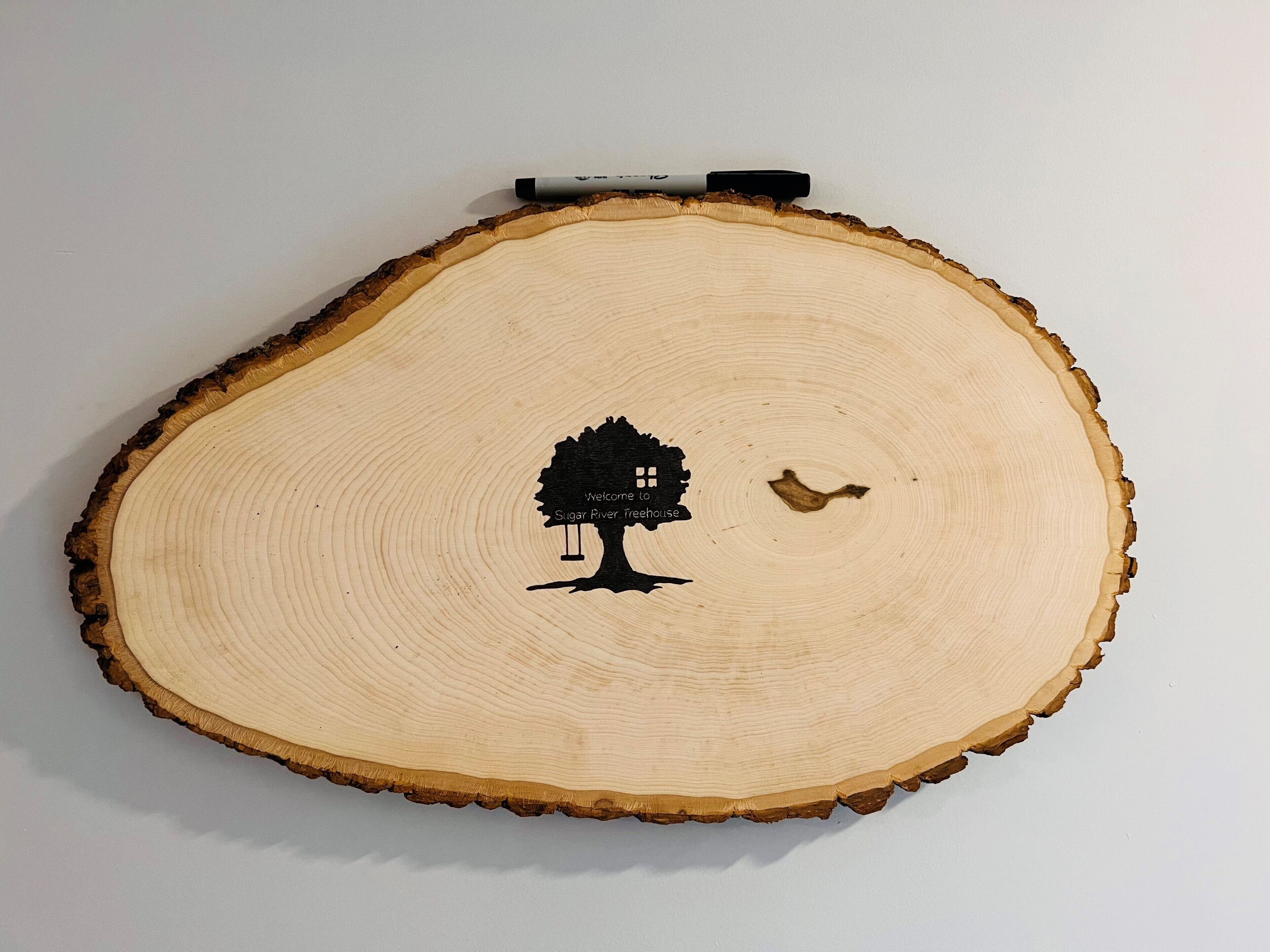 Una rebanada de madera con el silueta negra de un árbol y un pájaro, y un marcador encima.