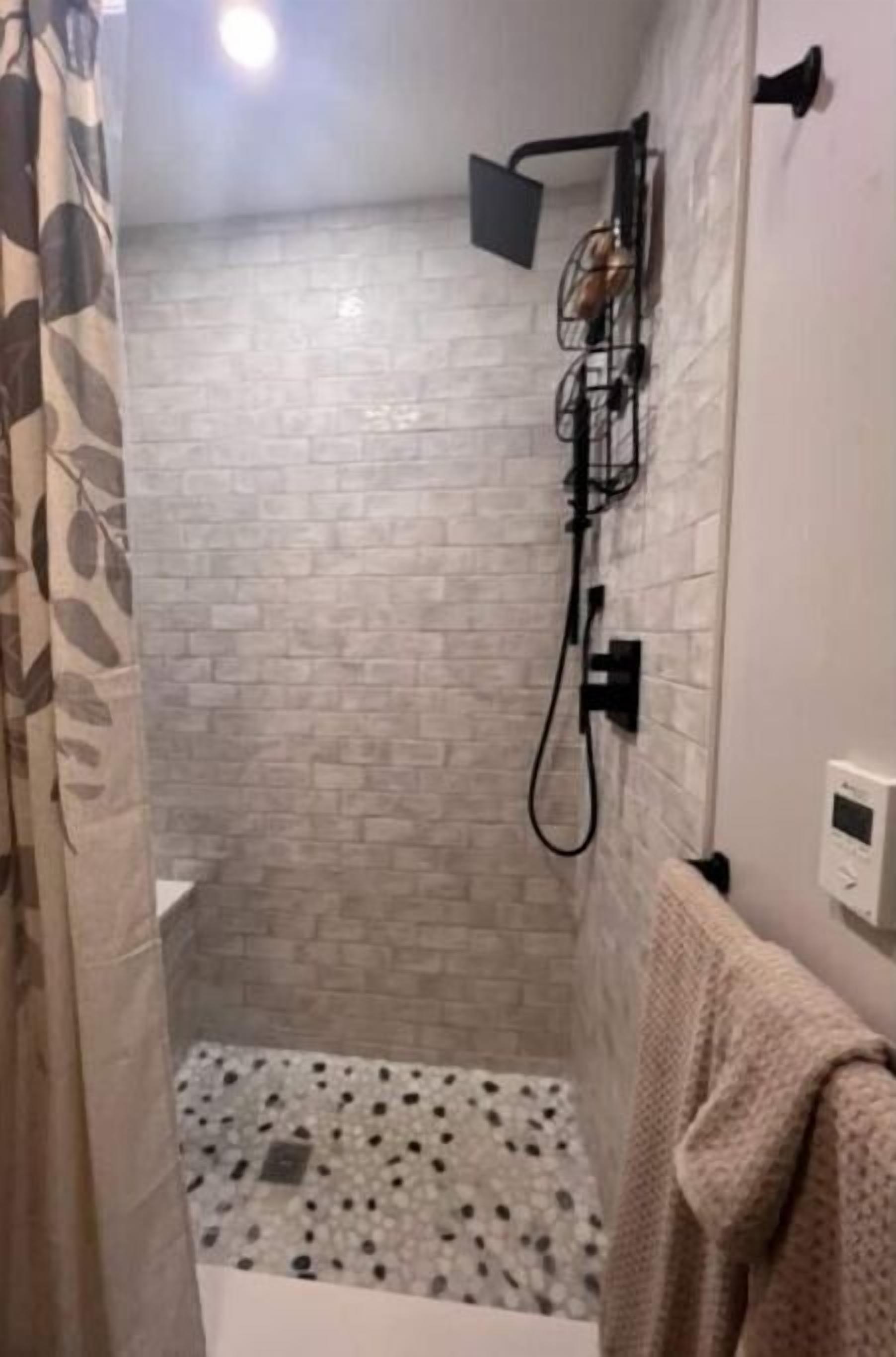 A shower area with a tiled wall, a showerhead, and a control panel.
