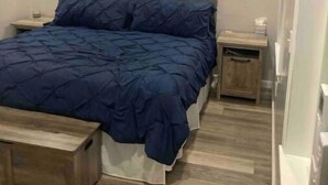 Un dormitorio con una cama grande, una mesita de noche, un banco de madera y una lámpara en el techo.