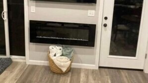 Una habitación con un televisor de pantalla plana grande montado en una pared blanca, una chimenea debajo y una cesta tejida en el suelo.