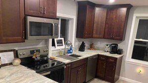 Una cocina con gabinetes de madera oscura, un microondas de acero inoxidable, una estufa y un lavamanos.