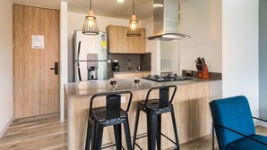 A modern kitchen with a central island, bar stools, a coffee machine, and a stainless steel range hood. - Go Living and Suites by Jalo (Medellín)