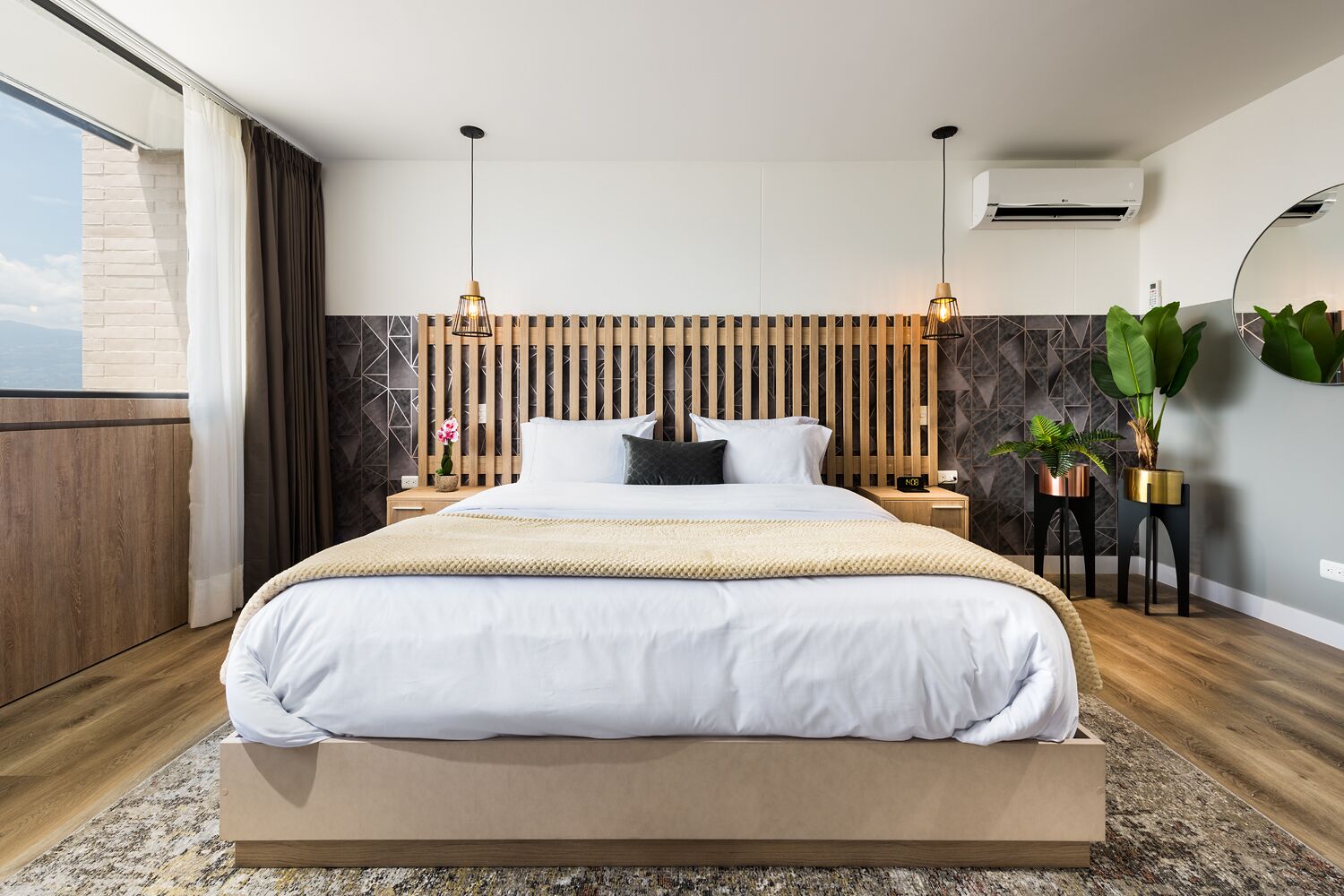 A modern bedroom with a large bed, wooden headboard, bedside tables, and a view of the outdoors.