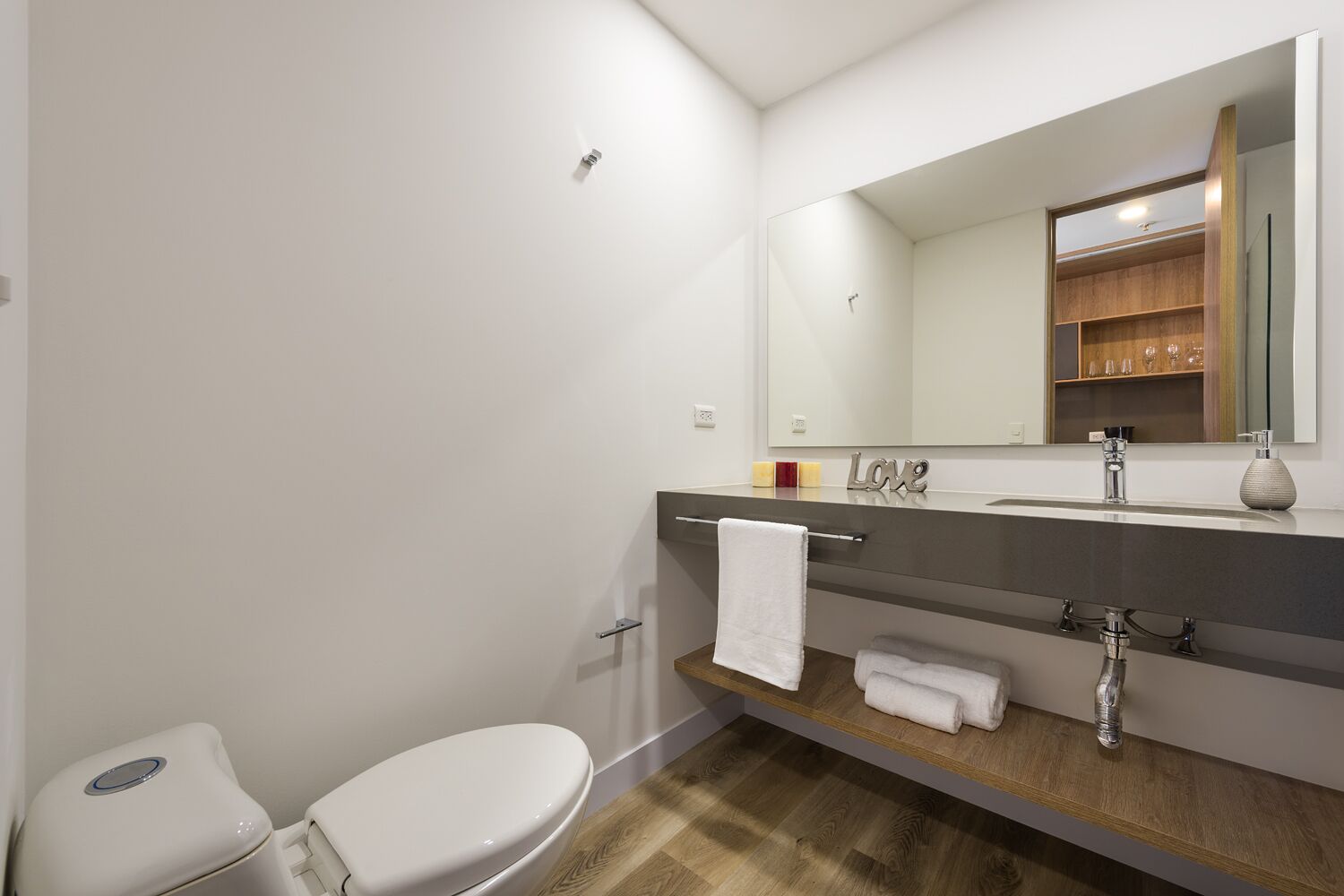 A modern bathroom with a white toilet, a vanity with a mirror, and a shelf with towels.