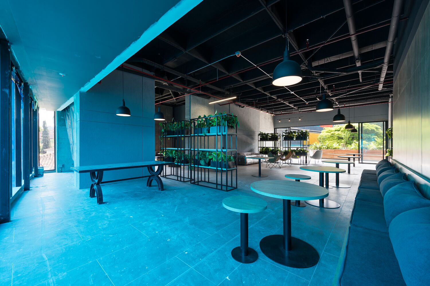 A modern indoor space with a high ceiling, exposed ductwork, and a mix of seating areas including tables and a sofa.