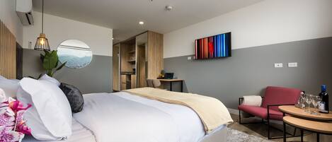 Une chambre d’hôtel moderne, dotée d’un grand lit, d’un bureau, d’une chaise et d’un téléviseur fixé au mur.