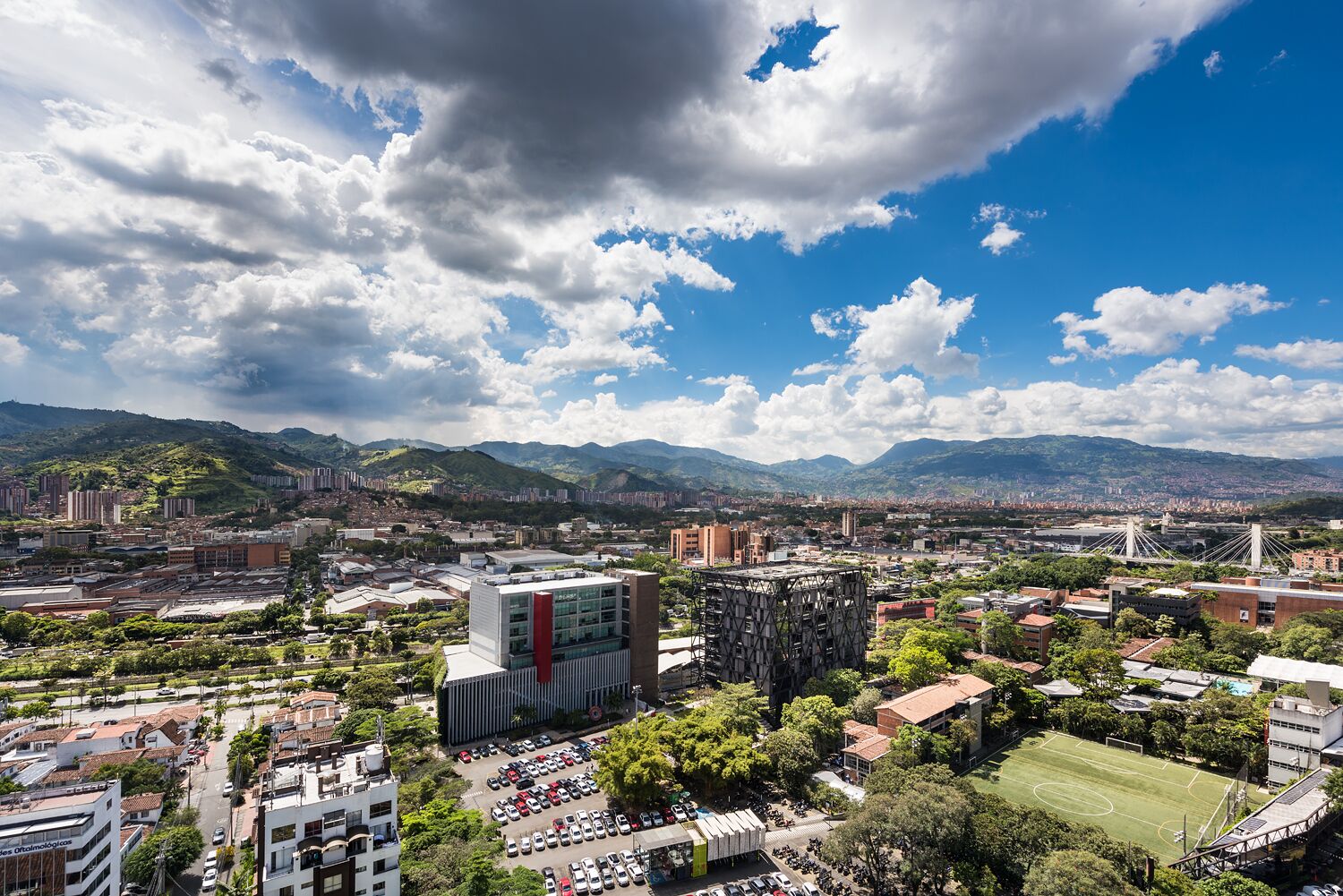 A cityscape with modern buildings, a large bridge, and a mountainous backdrop.