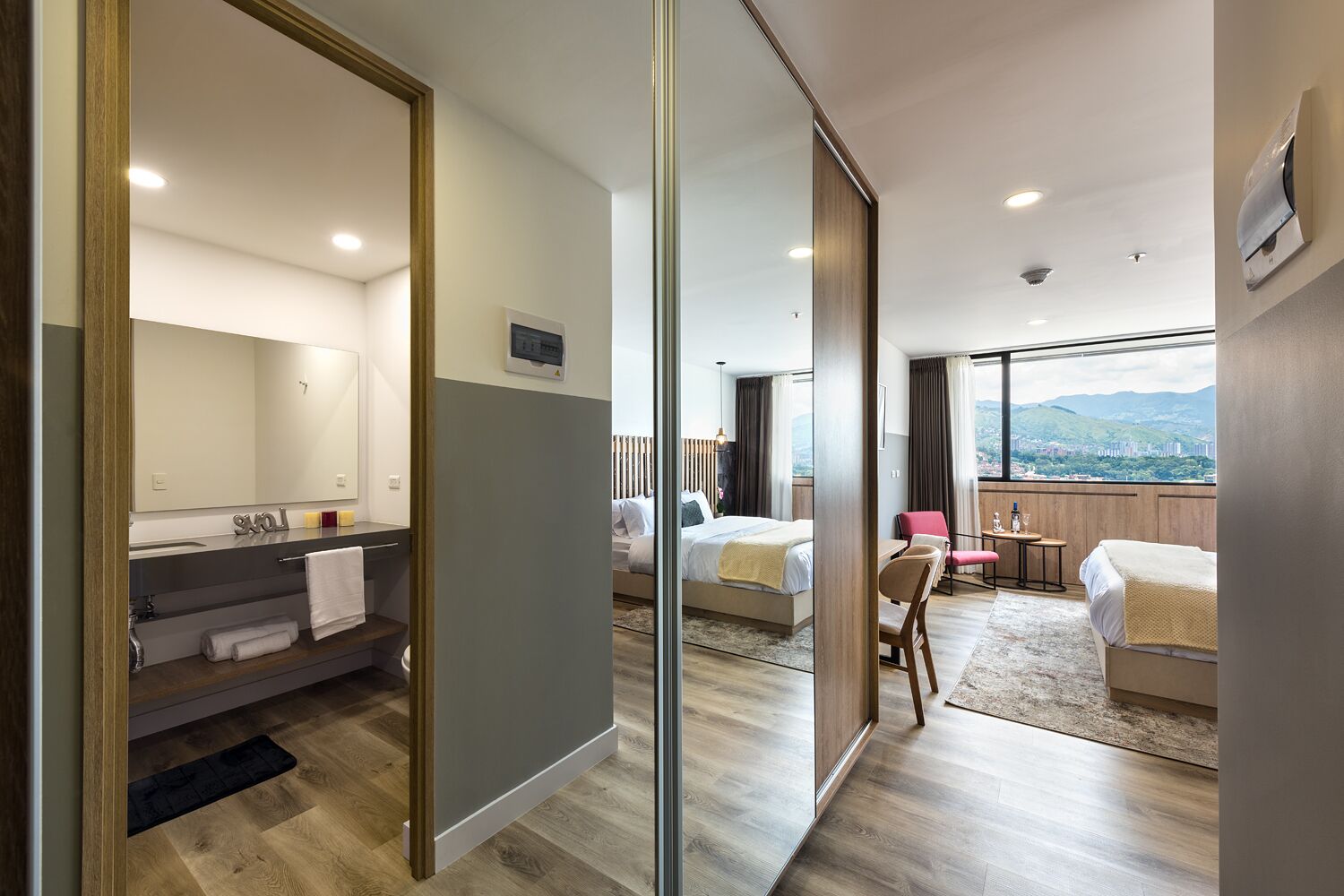 A modern hotel room with a large bed, a desk, a chair, and a view of the city.