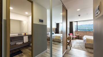 A modern hotel room with a large bed, a desk, a chair, and a view of the city.