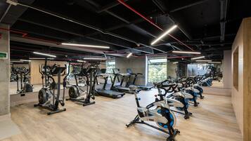 A gym with multiple exercise machines, wooden flooring, and a large window providing natural light.