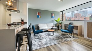 A modern living room with a sofa, two armchairs, a coffee table, and a city view through large windows. - Go Living and Suites by Jalo (Medellín)