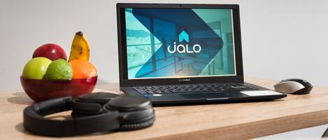 A laptop on a wooden desk with a bowl of fruit, a pair of headphones, and a mouse.