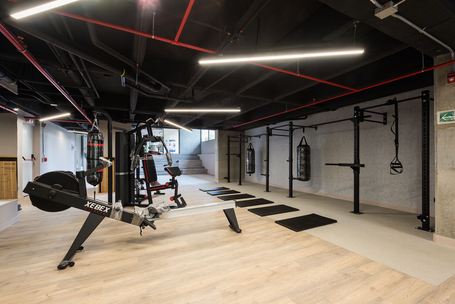 A gym with exercise equipment, wooden flooring, and a staircase in the background.