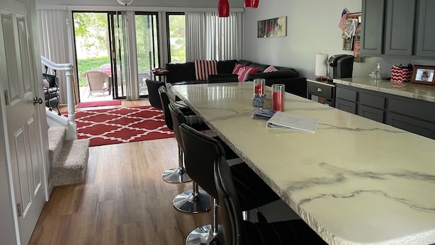 Een moderne keuken met een marmeren aanrecht, zwarte barstoelen en rode hanglampen.