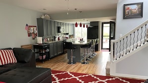 Een moderne keuken met grijze kastjes, een centraal eiland met barkrukken en een eetgedeelte met een vloerkleed met een rood patroon.