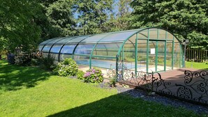 A greenhouse structure with a curved roof, surrounded by a well-maintained garden with various plants and flowers. - DOMAINE DES GRAVIERS (Plainfaing)