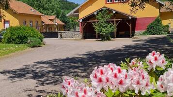 A yellow building with a red roof, surrounded by greenery and flowers.