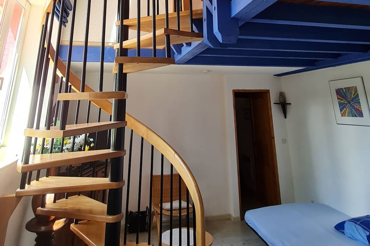 A spiral staircase with wooden steps and black railings, leading to a lofted sleeping area with a blue railing.