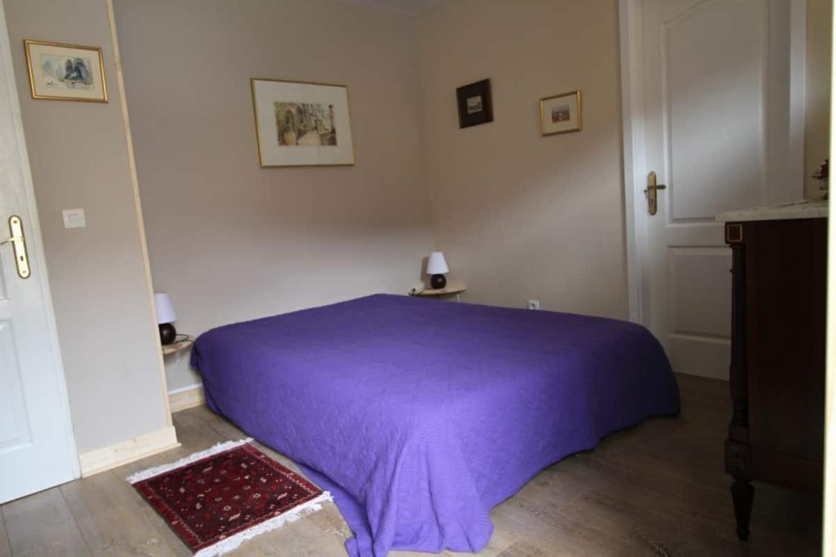 A bedroom with a bed, a nightstand, a lamp, and a door.