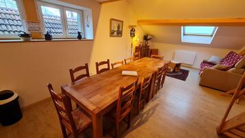 Un comedor con una mesa y sillas de madera, un sofá, una ventana con vistas a un tejado de tejas y una lámpara.