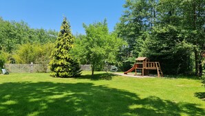 A backyard with a wooden play structure, a large evergreen tree, and a wooden fence. - DOMAINE DES GRAVIERS (Plainfaing)