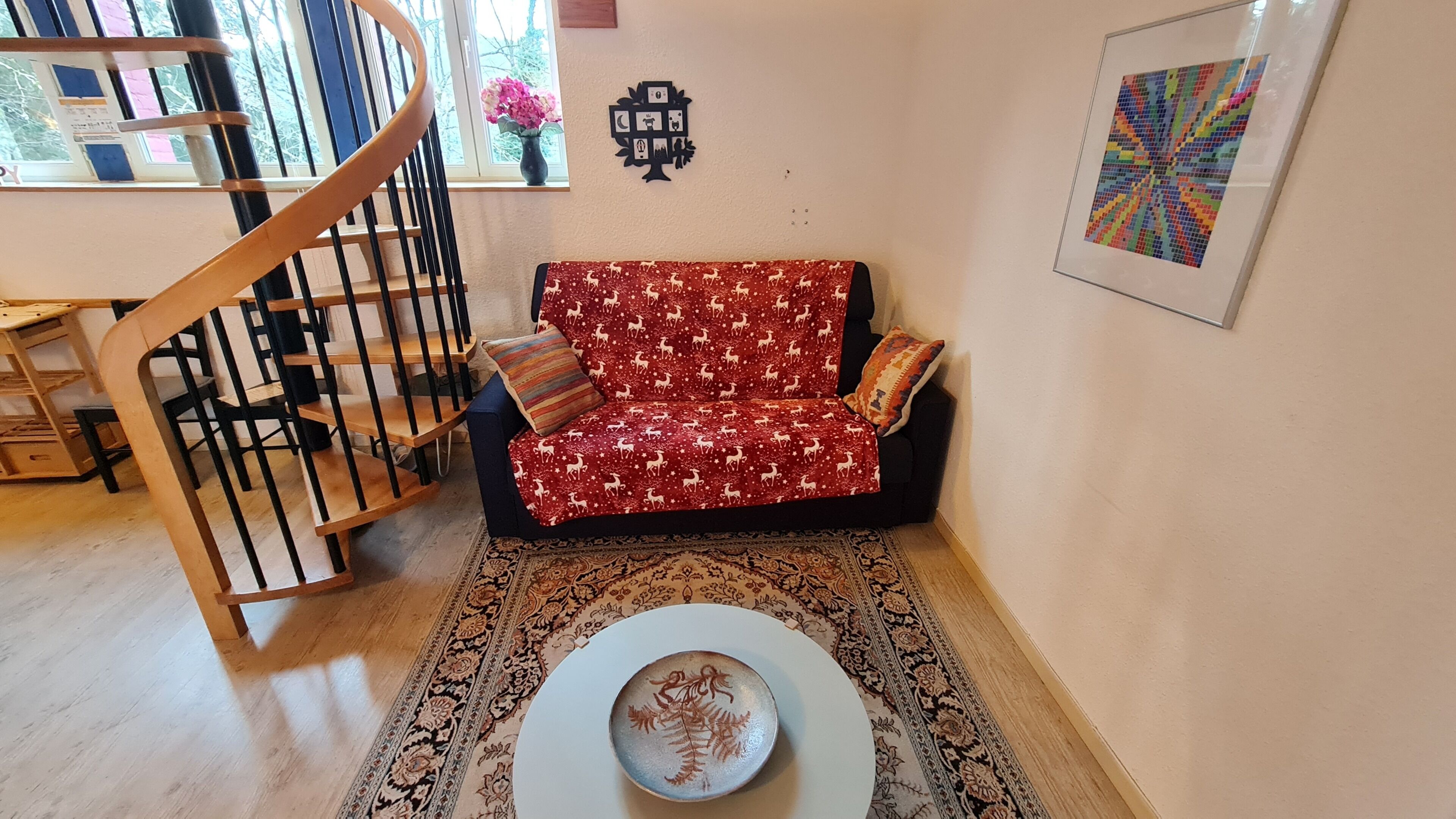 Een woonkamer met een bank, een bijzettafeltje, een trap en een wanddecoratie.