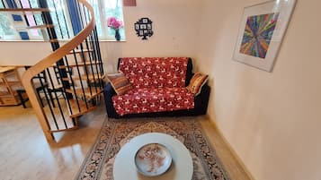 Een woonkamer met een bank, een bijzettafeltje, een trap en een wanddecoratie.