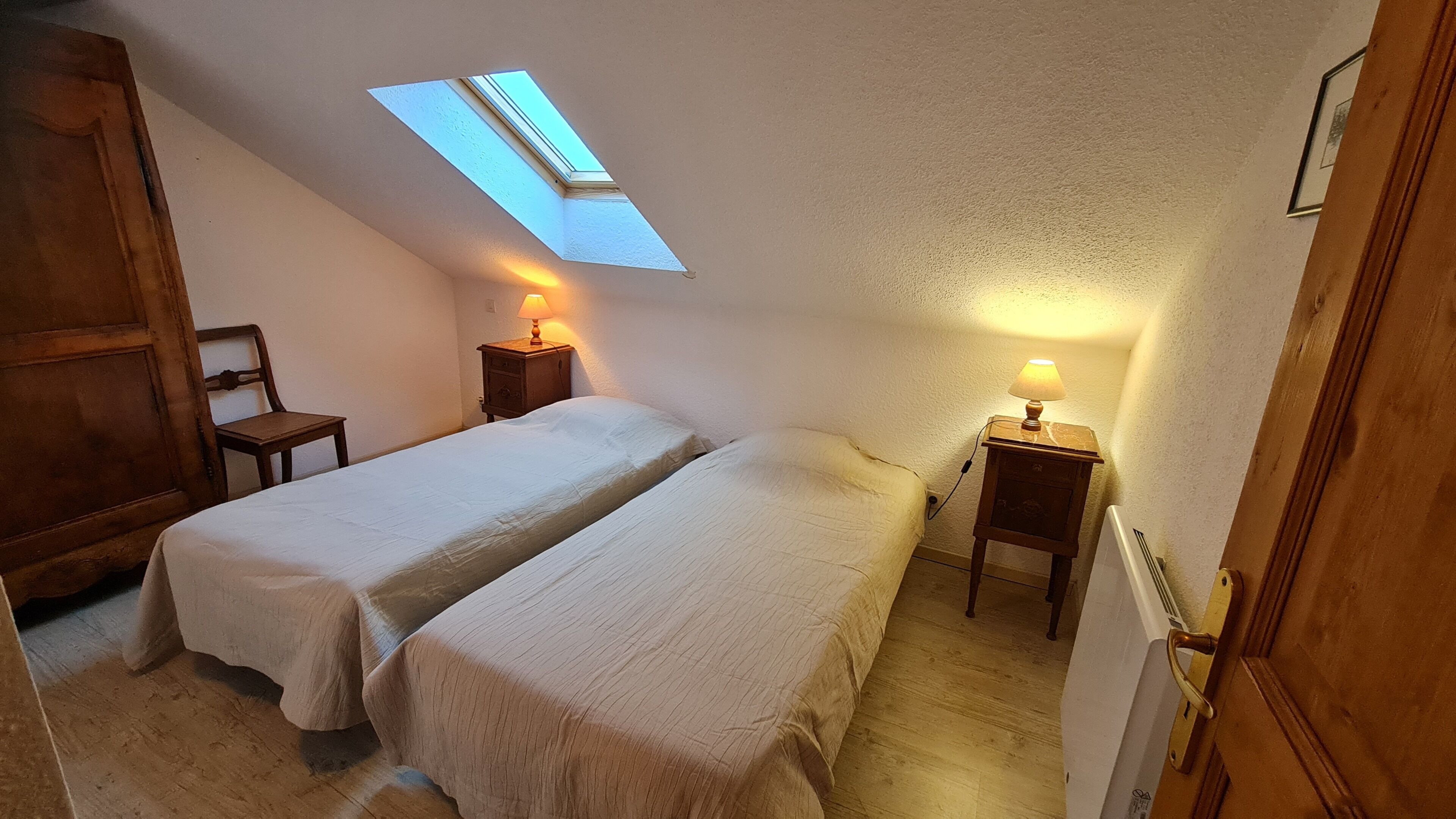 Une chambre avec deux lits, une lucarne et des lampes de chevet.