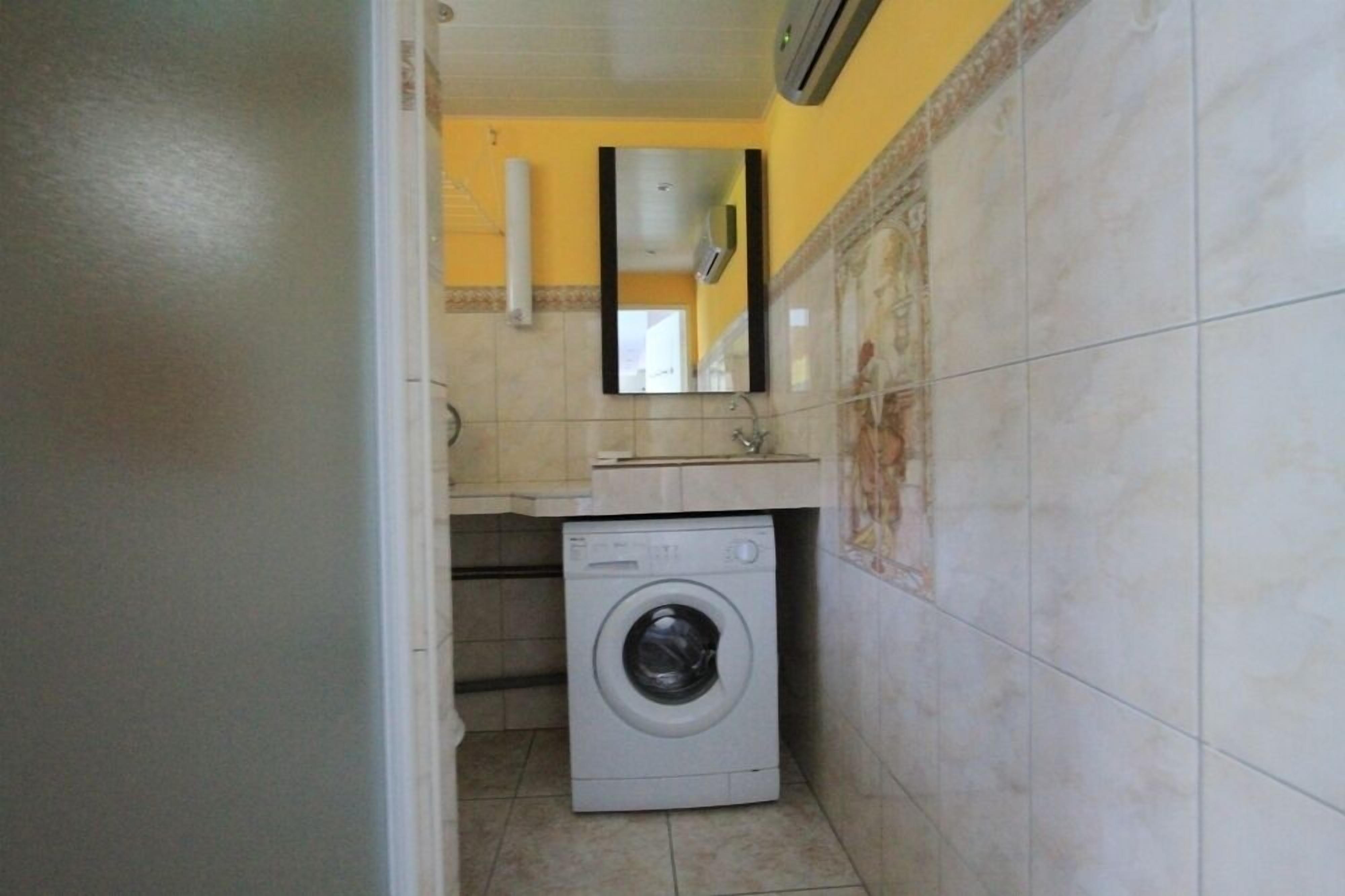 A compact laundry room with a washing machine, a sink, and a mirror.